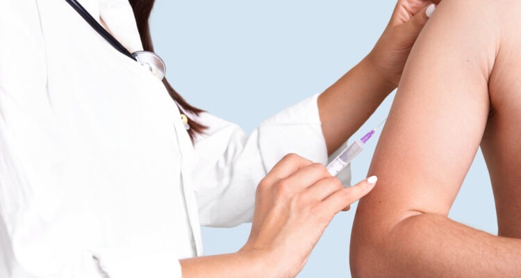 Close up shot of female doctor`s hands makes vacciantion to patient, uses syringe, inject at upper arm, prevents serious disease, isolated over blue background. Selective focus. Heathcare concept